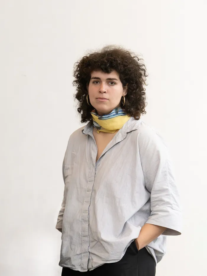 Portrait of a woman with short curly hair and a scarf, standing against a white background.