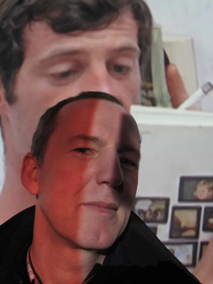 Portrait of a man with part of his face overlaid by a projection, with a large projected image in the background.