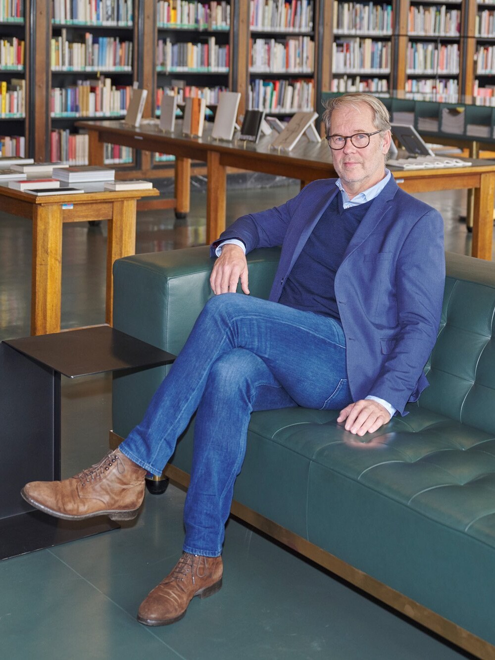 Mann sitzt auf einem Sofa in einer Bibliothek, umgeben von Bücherregalen und Ausstellungstischen.