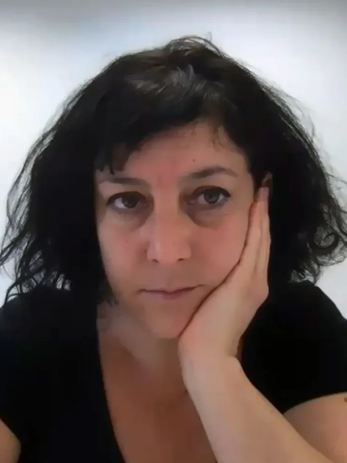 Eine Frau mit kurzen dunklen Haaren in einem schwarzen T-Shirt stützt ihren Kopf auf ihre Hand und blickt in die Kamera.