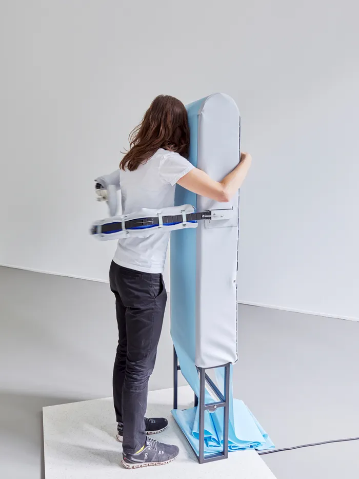 A person stands with their back to the camera, hugging an upright padded object mounted on a metal frame.
