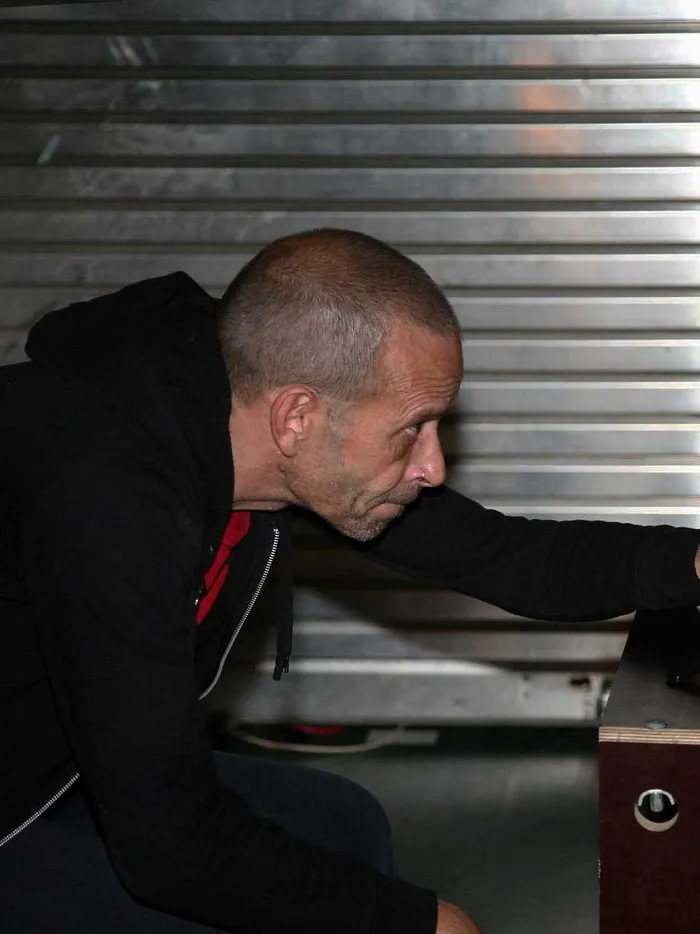 Man leaning forward to adjust a small camera on a tripod placed on a box, with a metal shutter in the background.