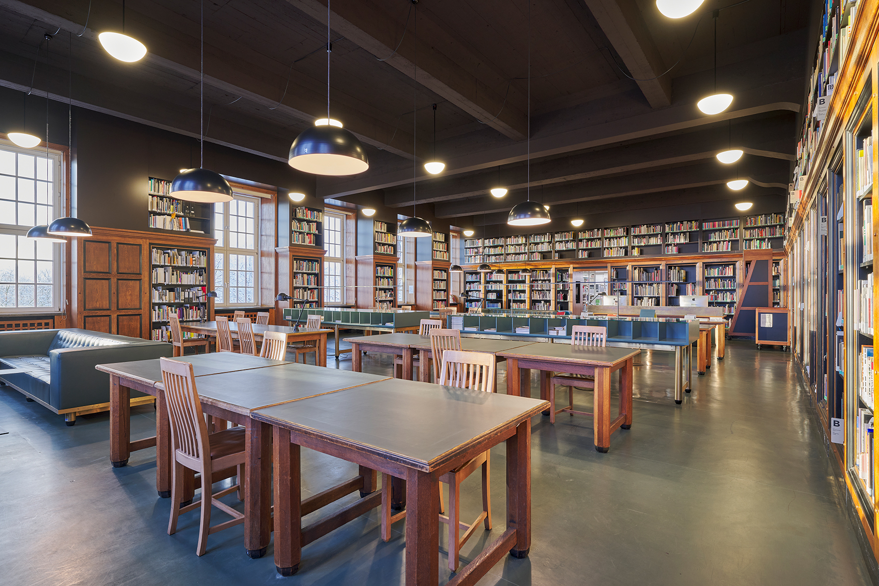 Tisch mit Computer, Sofas und Tisch mit Zeitungen, weitere Reihen von Tischen und Stühlen