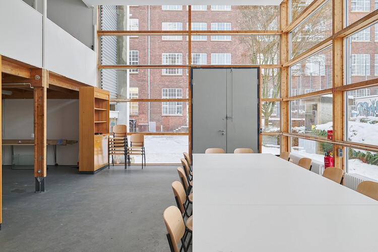 Ein Glaspavillon mit großen Fenstern, einem weißen Tisch in der Mitte und einer erkennbaren Empore an der Seite.