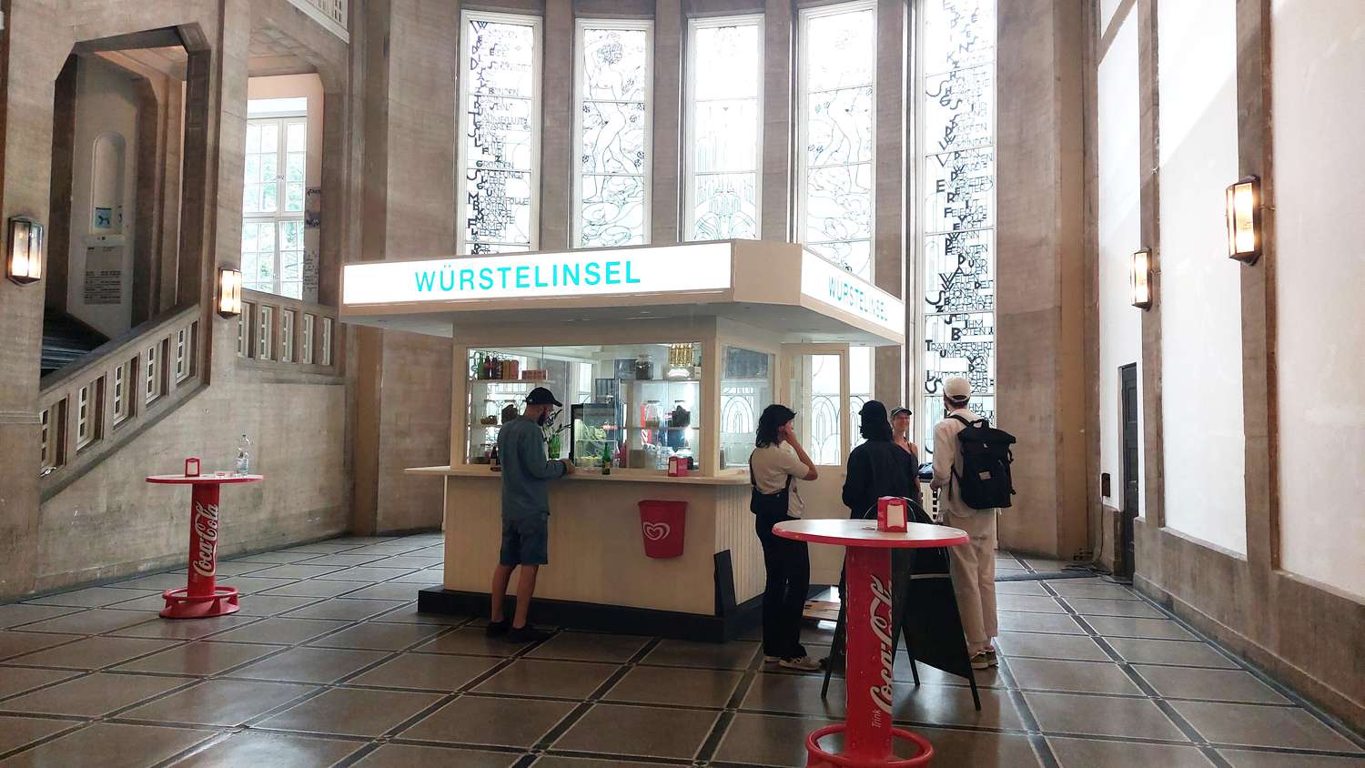 In der Eingangshalle der HFBK steht eine Holzbude mit dem hinterleuchteten Schriftzug "Würstelinsel". Davor stehen ein paar Leute.