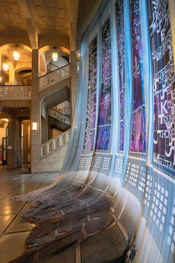 Das Hochformat zeigt den Vorhang in der Eingangshalle der HFBK vor der großen Fensterfront. Der Vorhang ist etwas zu lang und schleift mit ca. 1m über den Boden. Im Hintergrund ist das Treppenhaus zu sehen.